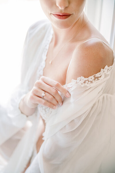 A romantic detail shot of a bride’s lace wedding gown and delicate gold engagement ring, captured at Dover Hall in Richmond, Virginia. The intricate floral appliqué on her sheer sleeve and the soft ivory tones of her bouquet evoke timeless elegance. Photographed by Caitlin Wilcox Photography, a luxury wedding photographer specializing in film and digital imagery.