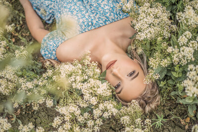 senior girl  in a blue dress laying in a field of white flowers