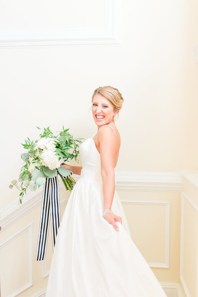 Bride posing on staircase with white and greenery bouquet with black and white striped ribbon