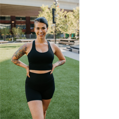 Woman with dark hair in black sports bra and biker shorts outside
