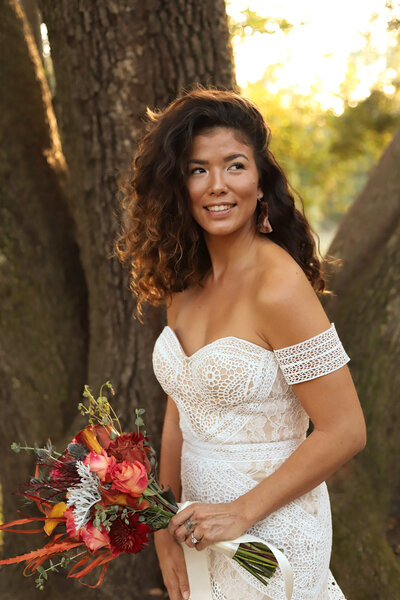 bride in a boho style dress with a bouquet standing by a tree in south carolina