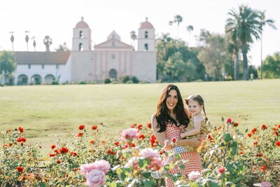 Mother and daughter in gingham dresses standing in a rose garden for their family photos
