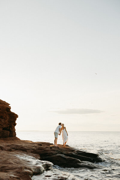 couple embrace next to ocean during lifestyle photos in pei