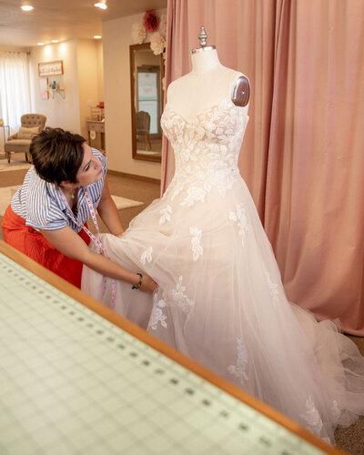 A seamstress delicately pinning details on a lace wedding dress in a studio