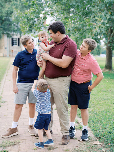 A man holding and looking at a baby while other children look at the baby at a Richmond mini session by Katie Stansfield Photography.