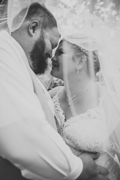 Black and white photo of bride and groom underneath veil touching noses by Iowa City wedding photographer Sabrina Wilham