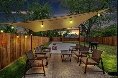 Backyard with outdoor seating and lighting at this three-bedroom, two-bathroom home with fully stocked kitchen, large backyard, grill, and basketball hoop in downtown Waco, TX.