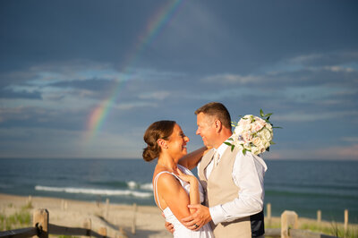 bride and groom smile under rainbow in Beach Haven
