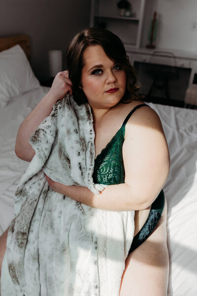 stunning woman in green lingerie grasping a fur blanket over her body and looking confident captured by Wisconsin Boudoir Photographer Ashley Kalbus