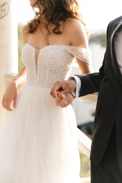 Romantic wedding portrait with couple holding hands showcasing their rings and wedding attire.