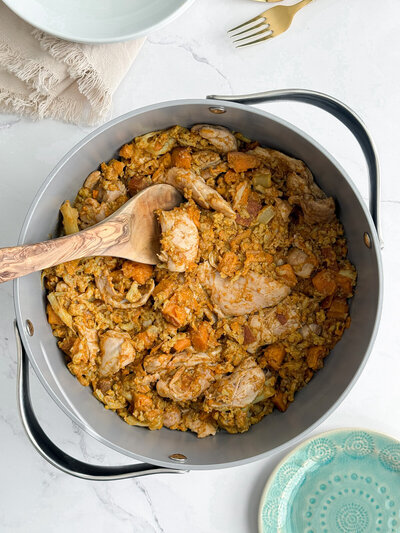 A pot of chicken vindaloo with sweet potatoes and cauliflower, on a marble counter next to a turquoise plate.