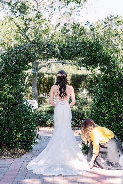 a bride facing away from the camera and a wedding planner fluffing her dress