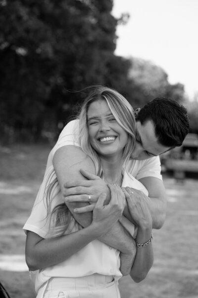 Candid black and white engagement photo of a joyful couple embracing outdoors, captured by editorial couples photographer Madison