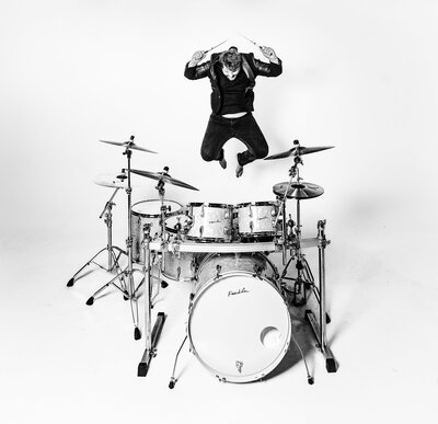A drummer playing his drums jumping in the air, photo in black and white.