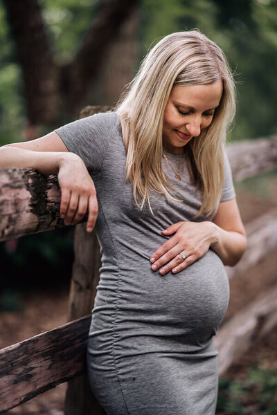 A pregnant mother leans back against a fence near Lake Harriet in Minneapolis, during a maternity lifestyle photography session.