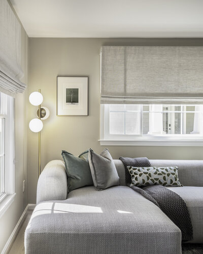 neutral living room with new window and window treatment, custom pillows, brass and globe floor lamp, brown throw blanket, artwork