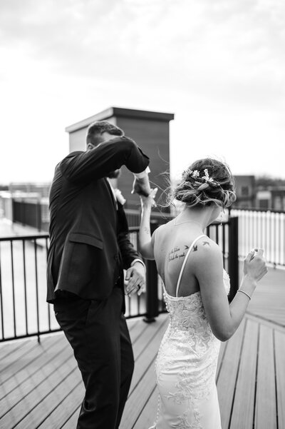 Black and white portrait of a bride and groom dancing on rooftop.