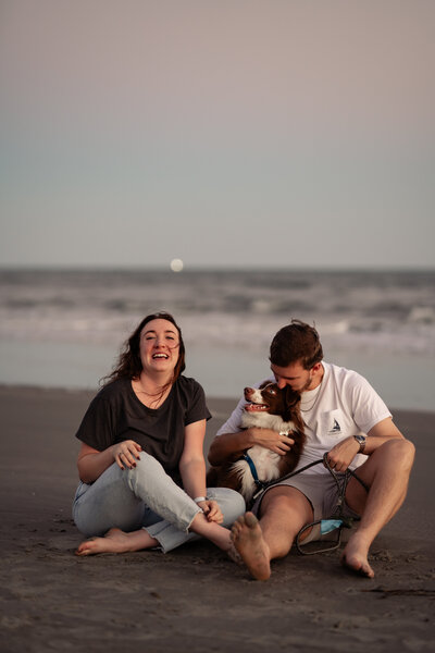 Couple on the beach at blue hour with their dog sitting in the sane together. 