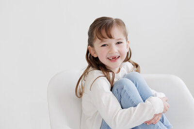 Little girl missing two front teeth sitting in chair at boise photography studio during child photos with Tiffany Hix
