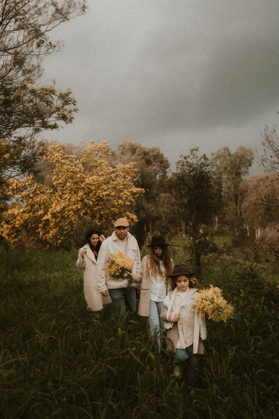 une famille de quatre marche dans les herbes hautes au milieu des mimosas en fleurs a cannes