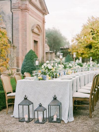 a long table scape outside of a Villa in Tuscany Italy with lanterns and florals on the table and ground