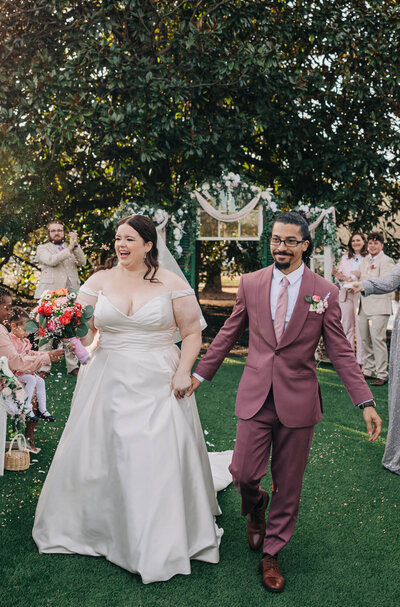 Couple smiling and holding hands while  walking back down the aisle after their ceremony