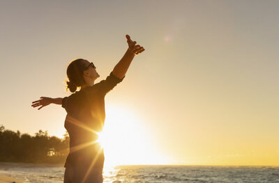 woman at the beach with arms extended during sunset