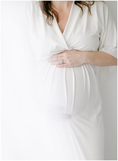 mother in white dress holding her pregnant belly