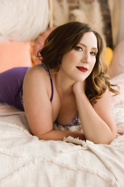 Smiling at the camera, women lays on bed in purple lingerie