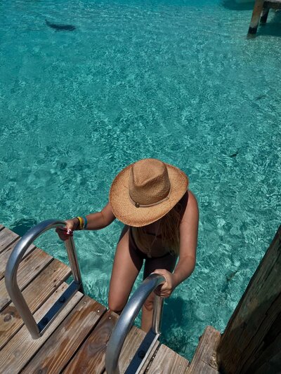 A woman climbing out of turquoise water onto a dock