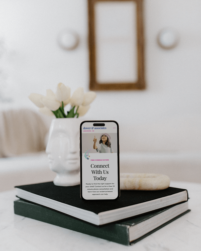 A smartphone displaying a "Connect With Us Today" webpage—crafted by Sweet Pea Ink Creative—stands on two stacked books next to a white vase with tulips on a marble table.
