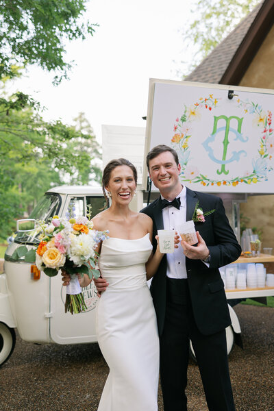 Bride and groom standing in front of truck smiling with drinks