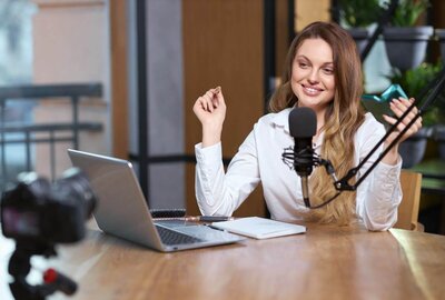 Happy woman podcaster speaking into a microphone and facing a laptop
