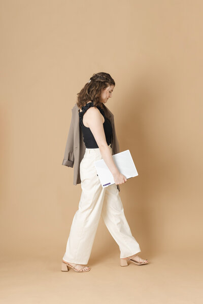 a woman walks across the frame holding her laptop casually in her hand