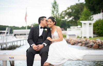 groom kisses bride's cheek on lakeside dock