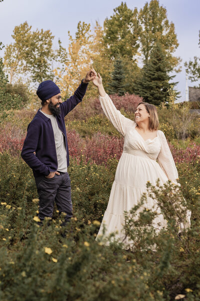 Man twirls his fiance amongst flowers during their engagement shoot