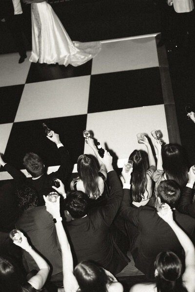 A look down in black and white of a wedding party raising drinks during the first dance