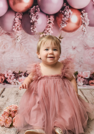 little girl in pink dress posing in front of pink and gold balloons and flowers