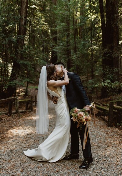 Newlyweds sharing a kiss in Armstrong Redwoods State Park on their wedding day