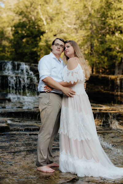 bride and groom standing together with a waterfall in the background and green trees