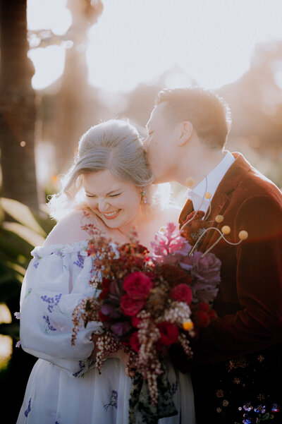 Groom in a red velvet jacket kissing his bride