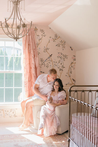 husband kissing wife holding newborn baby in home nursery 
