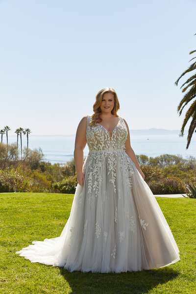 Bride in a sleeveless floral-appliqué A-line wedding gown standing on a lawn with ocean views