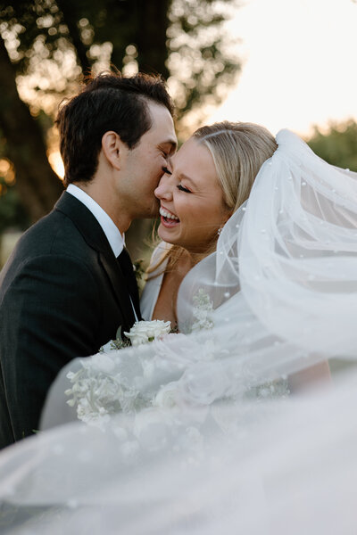 groom whispering in brides ear while she laughs