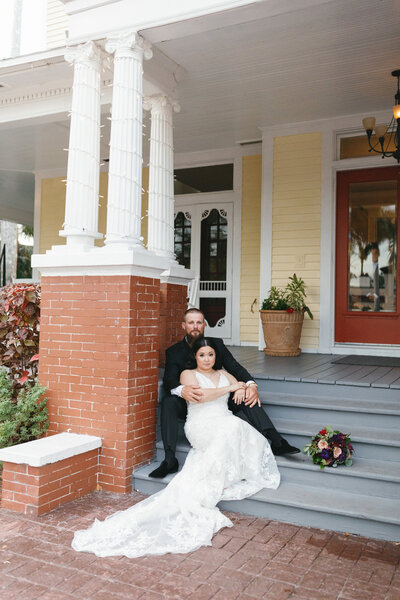 couple sitting on the front steps of the house posing for their wedding portraits