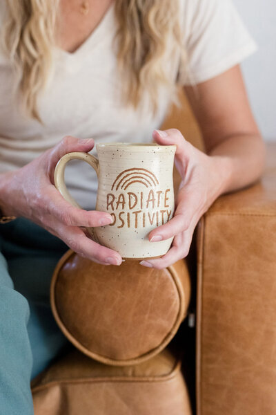 Amy holding a ceramic mug with the words "Radiate Positivity" 