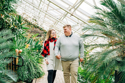 A couple walks together during their engagement photos in Ohio at a botanical garden.