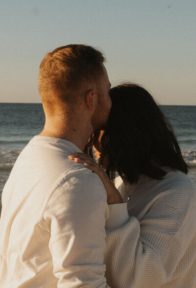 Man kissing a girl on the forehead with the ocean in the background at sunset