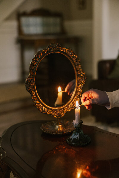 Hand lighting a candle with the reflection in a gold mirror
