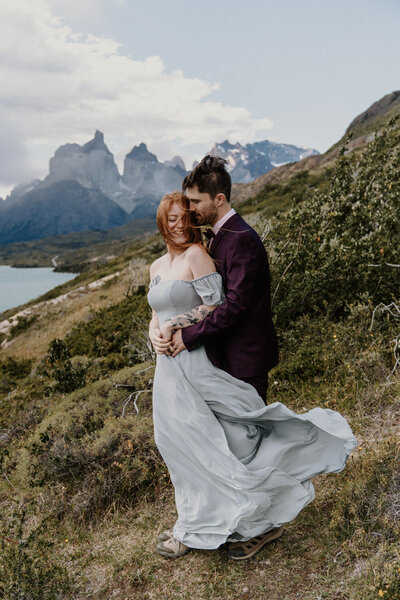 An eloping couple wearing a red dress and grey suit looks out  over Eibsee near Garmisch
